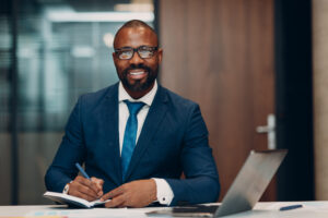 Portrait Smiling African American Businessman Signs Contract Sit Table Meeting Office With Notebook With Pen Laptop